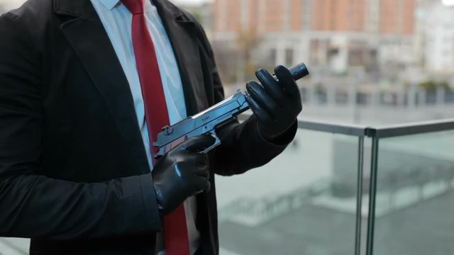 Hands of the assassin are screwing the muffler to the gun, he is preparing a murder.