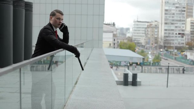 Man looks at the city from the roof of the house and talks on the phone. In his hand is a gun, he is a member of the Mafia.