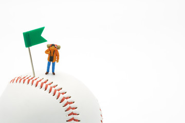 Miniature people standing with Green Flag Pin on baseball on a white background and red stitching baseball. as background travel concept and Business concept with copy space.