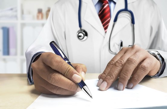 Doctor behind desk writing prescription for patient