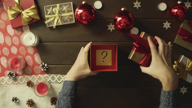 Man opens Christmas gift box with stick note with question mark on it, top down shot