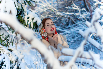 Beautiful European fashionable woman at winter, in a headscarf on her head, against the background of trees. Fairy-tale winter, Vintage red lips and bright eyes. Snow falls 