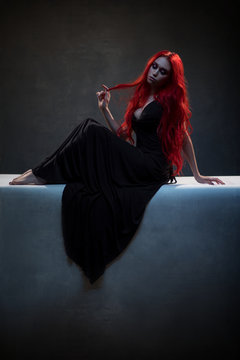 Beautiful red haired woman in black dress posing in gothic entourage