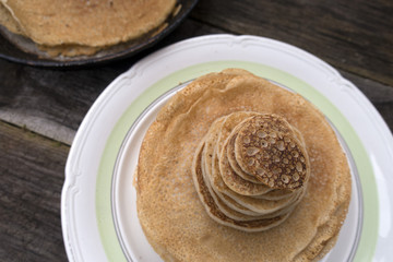 Large and small pancakes located on an old wooden table. Frying pan in which pancakes were prepared on the back of a fuzzy background.