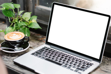 Mockup image of business woman using and typing on laptop with blank white screen and coffee cup on glass table in modern loft cafe, Soft focus on vintage wooden table.