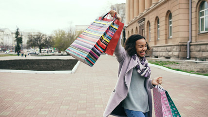 Attractive mixed race girl dancing and have fun while walking down the street with bags. Happy...