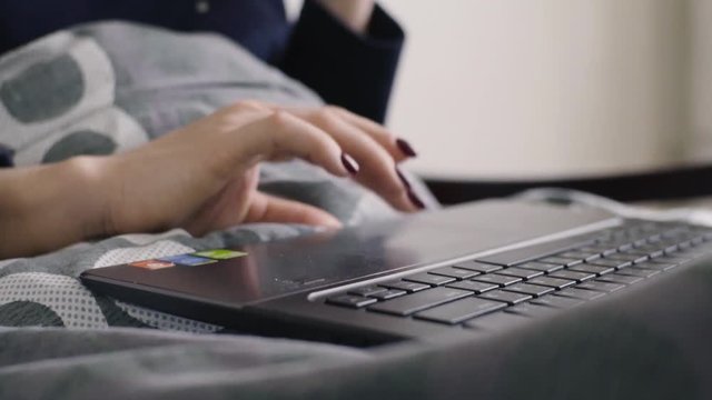 female hands working with laptop on comfortable bed close up