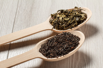 Two wooden spoons with dry leaves of black and green tea