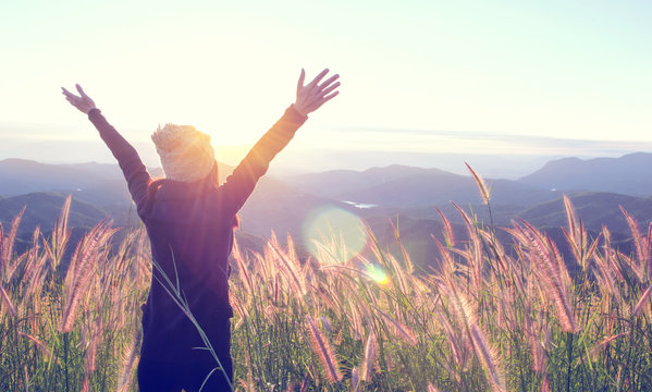 Happy Woman Enjoying Nature on grass meadow on top of mountain cliff with sunset outdoor. Freedom concept.