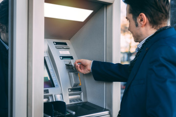 Businessman using cash machine and withdrawing money.