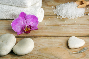 White towels, bath salts and stones for a hot massage on a wooden table.