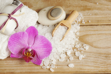 Obraz na płótnie Canvas Preparation for spa treatments, salt, towels, lotion and a bright orchid flower on a wooden table