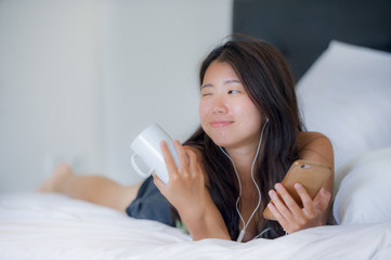 Obraz na płótnie Canvas young beautiful Asian Chinese woman with earpiece listening to music smiling happy lying on bed using internet on mobile phone