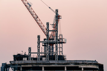 cranes on top of under construction high-rise building at twilight