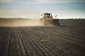 Naklejka premium Red tractor with sowing machine on a ploughed field