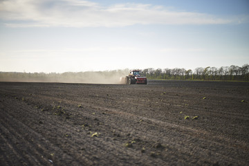 Naklejka premium Red tractor with sowing machine on a ploughed field
