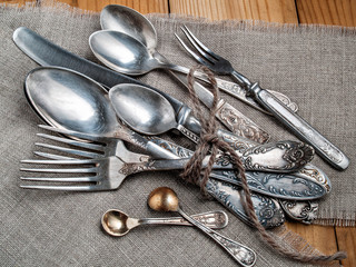 Old steel spoons, forks and knife, bound with twine lie on a napkin on a wooden background