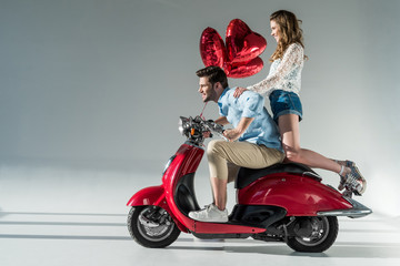 Fototapeta na wymiar side view of young couple in love with heart shaped balloons on red scooter