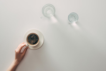 top view of female hand with cup of coffee and glasses with water on grey