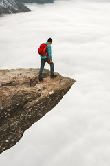 Tourist Man with backpack on Trolltunga rocky cliff edge in Norway mountains Travel Lifestyle wanderlust adventure concept vacations outdoor above clouds