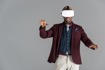 african american man using vr glasses with arm outstretched on grey background