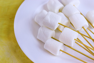 marshmallows on a sticks, laying on a white plate. prepared for fondue.