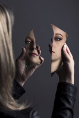 Woman looking at her face in two shards of broken mirror
