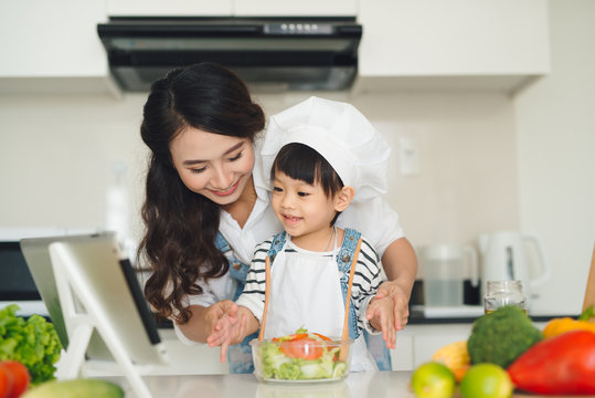 Mother with her daughter preparing lunch in the kitchen and enjoying together.