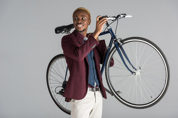 Fototapeta na wymiar smiling african american man holding bicycle in hands isolated on grey