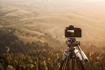 The camera on a tripod against the background of the mountains and the setting sun records video timelaps. Technology and travel.