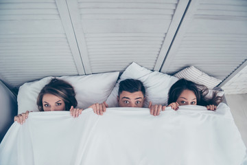 Top view of funny three partners hiding behind blanket, peeking over sheets and looking at camera while lying in bed at home, weekend, rest, relax, someone catches them