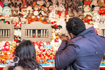 Back view of tourists playing shooting game to win plush toys on the wall at Christmas funfair...