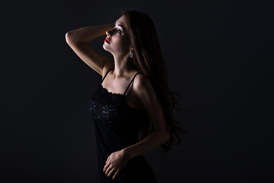 Woman with long curly hair, makeup, red lips and in jewelry in black dress