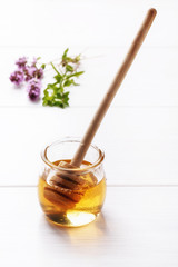 Honey in a small glass jar on a white table and honey dipper