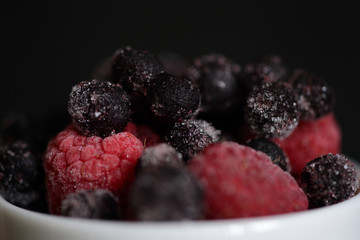 Frozen raspberries and blueberries on a dark background close up