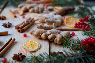 Powdered ginger, orange, anise, cinnamon, raw red viburnum berries on wooden background. Decorated with blurred Christmas tree branches and pine cones. New year composition. Still life. Flat lay