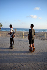 Boys are enjoying riding Monowheels scooters on a beach promenade © Olga