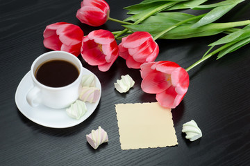 Fototapeta na wymiar Mug of coffee, marshmallows, blank postcard and pink tulips. Black background.