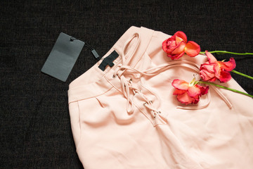 Pink trousers with drawstring on a black background, blank tag, roses. Fashion concept, close-up