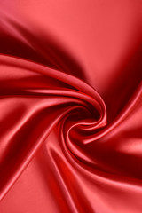 Close up of ripplesin shape of rose flower in red silk fabric. Satin textile background.