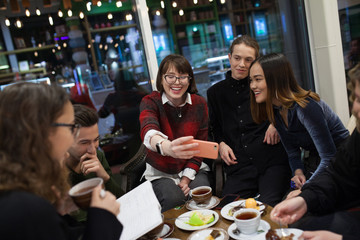 Group of positive teenagers make selfies and spending time in a cafe.