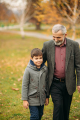 Fototapeta premium Grandpa and his grandson spend time together in the park. They are sitting on the bench. Walking in the park and rejoicing