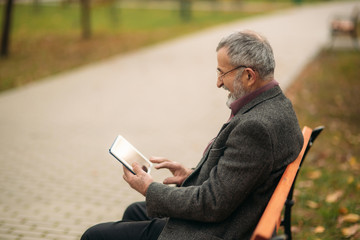 Fototapeta premium Grandpa use a tablet sitting in the pakr on the bench