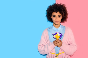 attractive african girl standing with flowers in hands on pink and blue background