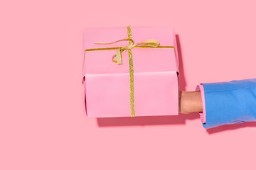 partial view of african american man holding wrapped gift on pink wall background