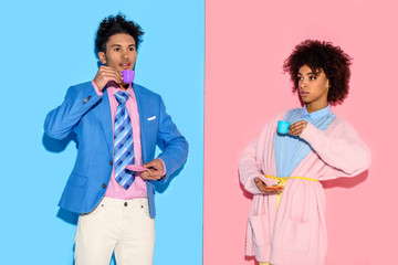 Fototapeta premium Stylish african american couple with toy teacups with pink and blue wall backdrop