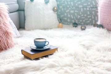 Cup of coffee and books on soft white carpet indoors