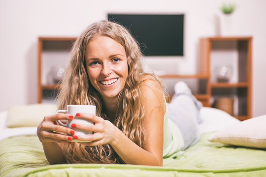 Young woman is lying in bed and drinking tea. 