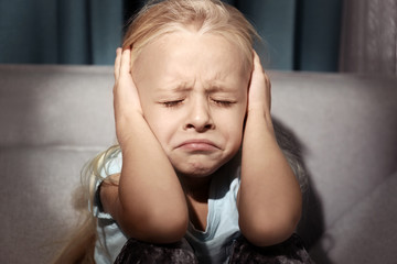 Helpless little girl covering her ears indoors. Child abuse concept