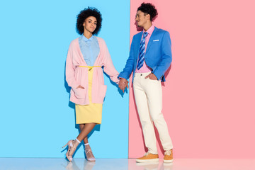Young african amercian smiling girl and guy holding hands on pink and blue background